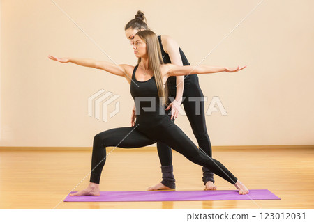 Instructor is helping young woman make yoga asana at gym. Instructor is helping young woman make yoga asana at gym. 123012031