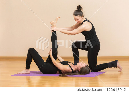 Yoga trainer is helping young woman make exercise stretching her leg at gym background. 123012042