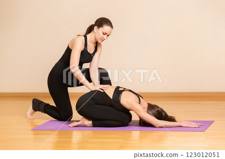 Fitness trainer is teaching young woman an exercise on a mat at studio background. 123012051