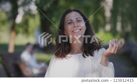 A joyful woman in a bright white outfit enjoys a sunny day in the park, radiating positivity around her 123012415
