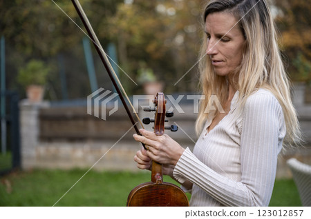 Woman tuning a violin in a peaceful outdoor setting Woman tuning a violin in a peaceful outdoor setting 123012857