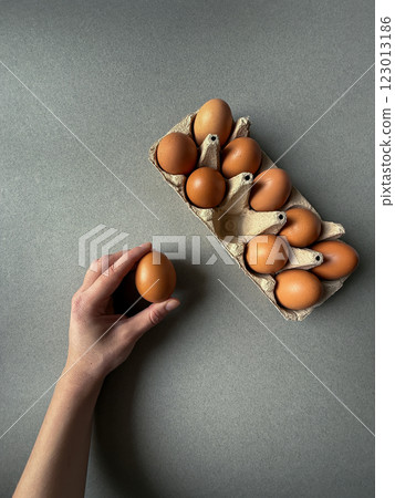 Brown chicken eggs in paper tray on grey background with a hand keeping one egg Brown chicken eggs in paper tray on grey background with a hand keeping one egg 123013186