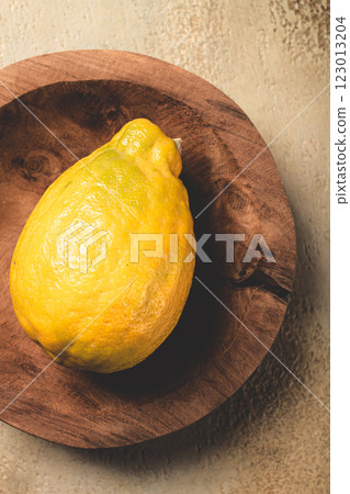 Bright yellow lemon resting on a wooden plate against a textured background in natural light 123013204