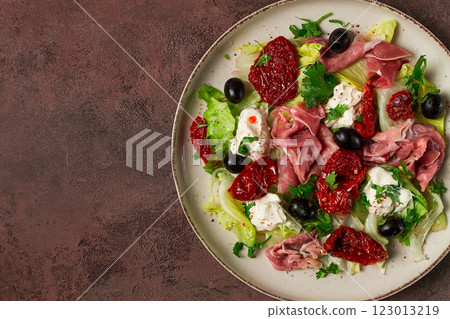 salad with dried tomatoes, prosciutto, soft cheese, olives, homemade, top view, 123013219