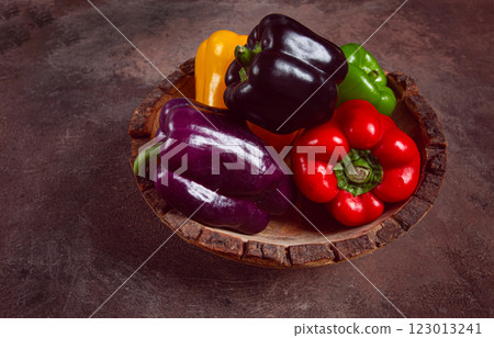 A collection of colorful bell peppers, in a wooden bowl, on a dark surface, top view, no people 123013241