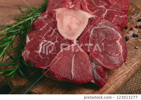 knuckle on the bone, raw meat for ossobuco, on a wooden chopping board, with a sprig of rosemary, and spices, top view, no people, 123013277