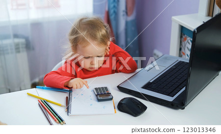 Cute baby girl at a desk with a laptop and calculator, focused on financial data. Freelance and distance work concept 123013346