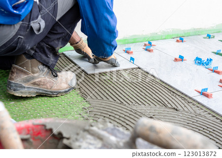 Piastrellista al lavoro installa un nuovo pavimento con le piastrelle. Edilizia. 123013872