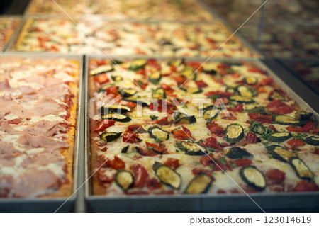 Authentic Italian pizza in a restaurant display window. Various pizzeria in glass window display. Focus on pizza with pepper and zucchini. View of slices of pizza in the restaurant 123014619