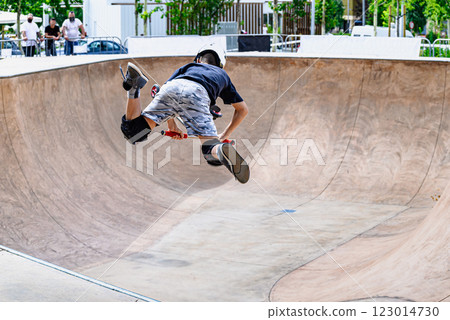 Young man practicing Scootering (Freestyle Scootering) in the new SkatePark in the central park of Igualada, Barcelona, blurred background 123014730