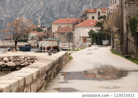 Picturesque coastal road lined with historic buildings and a moored boat in a serene bay of Montenegro 123015015