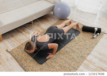 A woman does pushups on a yoga mat in her modern living room, promoting fitness and health A woman does pushups on a yoga mat in her modern living room, promoting fitness and health 123017696