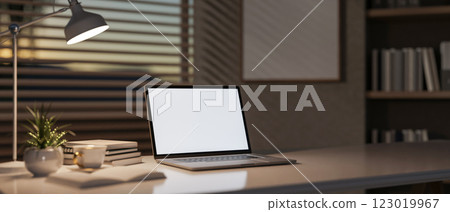 A laptop and decorative items sit on a table in a modern office, softly illuminated by a table lamp. A laptop and decorative items sit on a table in a modern office, softly illuminated by a table lamp. 123019967