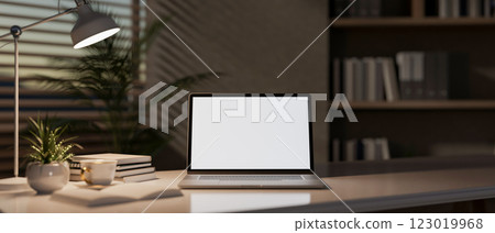 A close-up of a laptop sit on a table in a modern office, softly illuminated by a table lamp. A close-up of a laptop sit on a table in a modern office, softly illuminated by a table lamp. 123019968