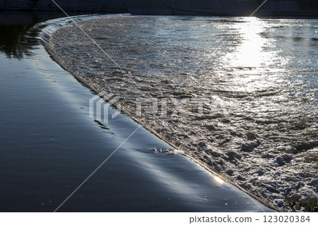 The morning sun reflecting on the rippling surface of the river 123020384