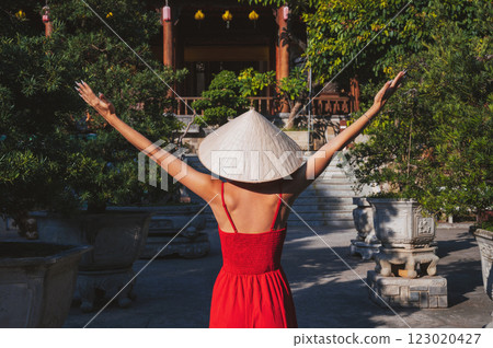 back of young woman tourist in a red dress and a traditional Vietnamese hat Non La at pagoda in Vietnam on a travel to Asia 123020427