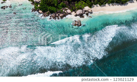 Turquoise waves crash against rocks along a scenic coast lined with lush vegetation. Seychelles, Mahe. 123021129