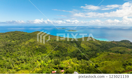 A scenic view of rolling green hills extending towards a calm turquoise sea under blue sky. Praslin, Seychelles. A scenic view of rolling green hills extending towards a calm turquoise sea under blue sky. Praslin, Seychelles. 123021139