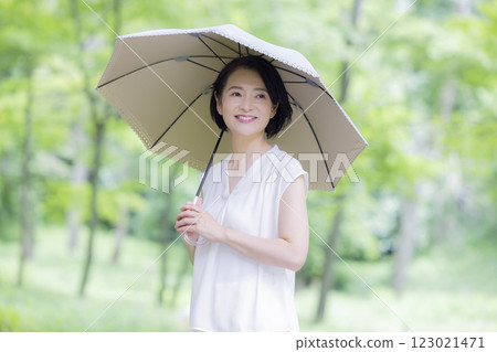 A middle-aged woman walking with a parasol among the fresh greenery A middle-aged woman walking with a parasol among the fresh greenery 123021471