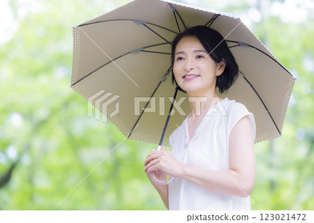 一位中年婦女撐著陽傘在新綠中行走 123021472