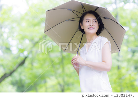 A middle-aged woman walking with a parasol among the fresh greenery 123021473