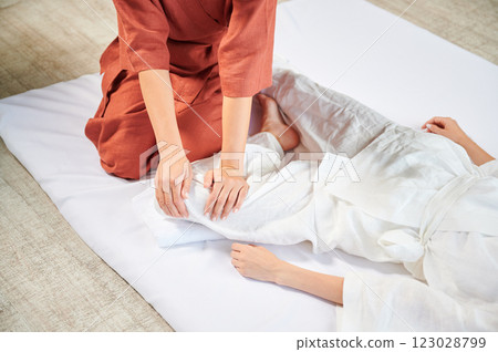 Masseuse making thai yoga massage. Woman therapist doing traditional massage treatment, stretching female patient's body. Client lying on mat, enjoying hand massage in calm atmosphere. Cropped view. 123028799