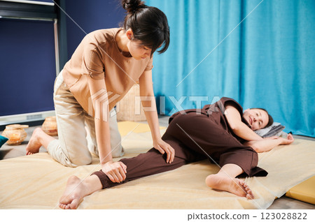 Masseuse making thai yoga massage. Woman therapist doing traditional massage treatment for female patient indoors. Client lying on mat, meditating, enjoying hand massage in calm atmosphere. Masseuse making thai yoga massage. Woman therapist doing traditional massage treatment for female patient indoors. Client lying on mat, meditating, enjoying hand massage in calm atmosphere. 123028822