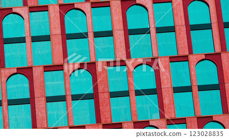The vibrant facade showcases a striking contrast between turquoise windows and red architectural frames. The diagonal perspective adds dynamism to the repetitive arched patterns 123028835