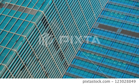 Two modern skyscrapers intersect at an angle, showcasing contrasting architectural styles. The repetitive grid patterns and blue-tinted glass create a dynamic urban aesthetic. 123028849