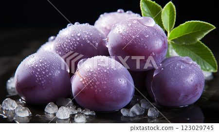 A close-up of fresh, purple plums with water droplets on their surface, accompanied by green leaves, against a dark background. 123029745