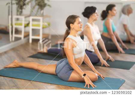 Girl stretching in seated asana Ardha Kapotasana at group yoga session 123030102