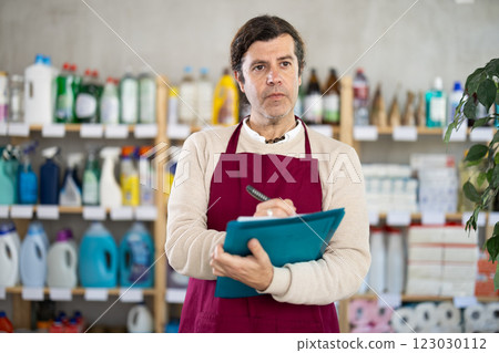 Man seller, with paper and invoice in hands, make inventory in store. Man seller, with paper and invoice in hands, make inventory in store. 123030112