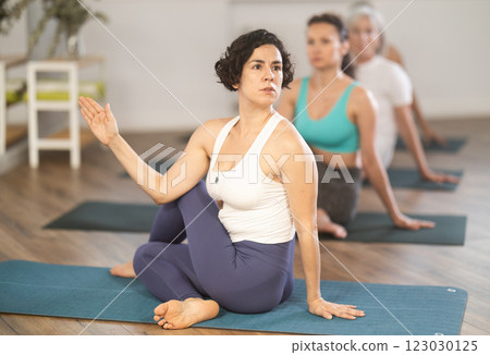 Hispanic woman performing seated twisting asana Matsyendrasana 123030125