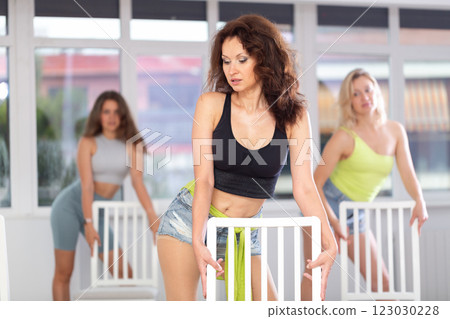 Young woman stands next to chair, leans on back and performs set of lap dance movements 123030228