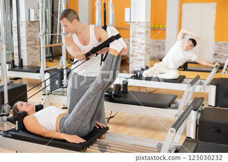 Girl athlete performs exercises to increase leg strength using sling reformer under coach guidance. 123030232