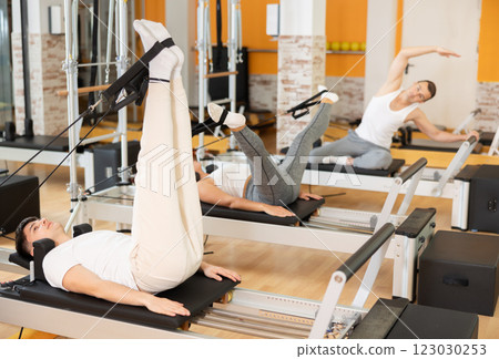Man works out in gym and performs set of exercises to stretch leg muscles with help of reformer 123030253