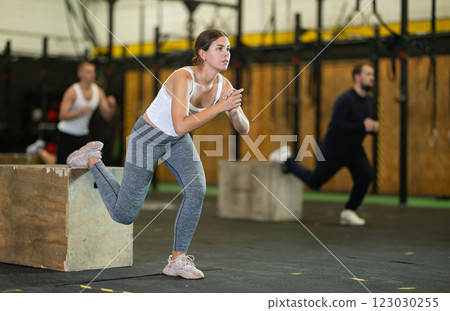 Concentrated girl performing Bulgarian split squats on box at gym Concentrated girl performing Bulgarian split squats on box at gym 123030255