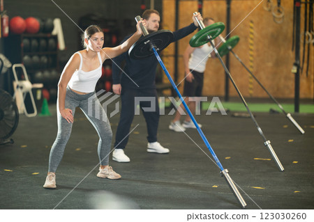Sporty girl doing one arm landmine press with barbell at gym 123030260