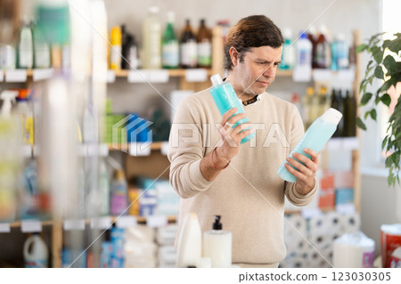 Man buyer chooses shampoo or shower gel in household goods department of supermarket Man buyer chooses shampoo or shower gel in household goods department of supermarket 123030305