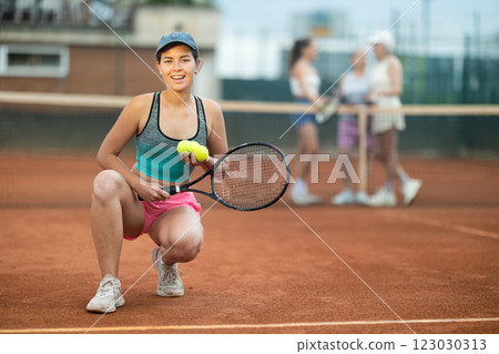 Smiling young female tennis player posing on outdoor court 123030313