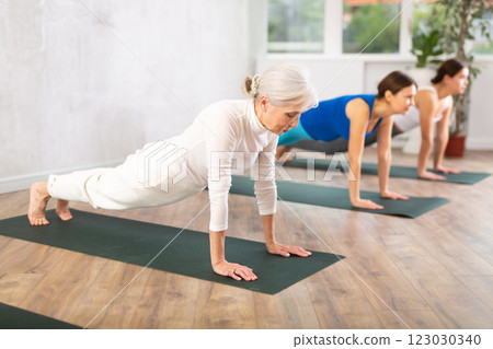 Focused older woman doing yoga poses with other women in yoga studio Focused older woman doing yoga poses with other women in yoga studio 123030340