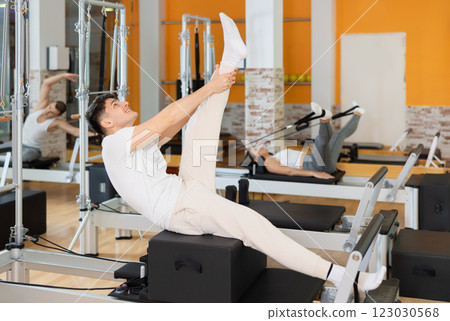Man works out in gym and performs set of exercises to stretch leg muscles with help of reformer 123030568