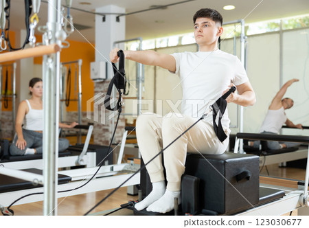 Guy doing exercises with straps on Pilates reformer using sitting box 123030677