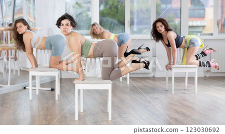 Woman sitting on knees on chair performs lap dance. Female students repeat erotic movements Woman sitting on knees on chair performs lap dance. Female students repeat erotic movements 123030692