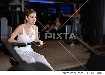 Sportive young girl training on cable row machine in gym Sportive young girl training on cable row machine in gym 123030801