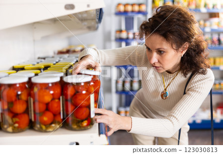 Adult woman chooses pickled tomatoes in store 123030813