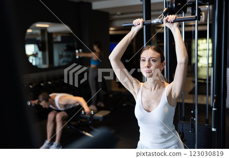 Slender athletic girl work out muscles of arms and shoulders on simulator in gym of fitness club Slender athletic girl work out muscles of arms and shoulders on simulator in gym of fitness club 123030819