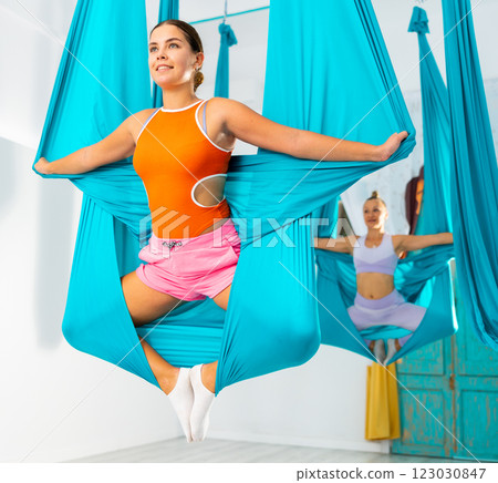 Girl performing butterfly pose holding hanging hammock with hands like wings Girl performing butterfly pose holding hanging hammock with hands like wings 123030847