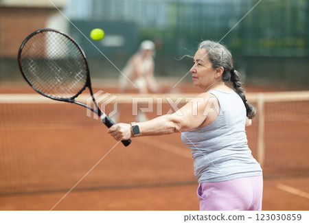Elderly woman engrossed in tennis game on clay court 123030859
