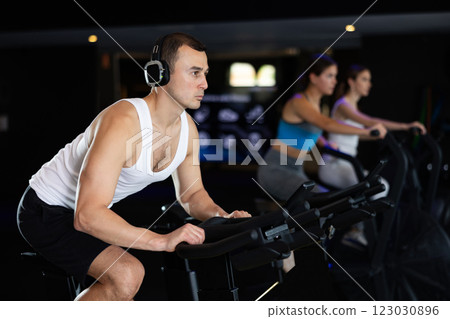 Sportive young guy doing spin bike exercises in well-equipped gym Sportive young guy doing spin bike exercises in well-equipped gym 123030896